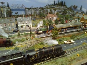 Model railroad landscape with houses, station, and people as well as bridges and hills in the background