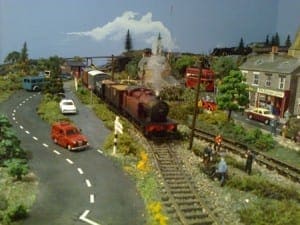 Cars driving on roads complete with signs and pedestrians alongside a model train in Japanese model railroad layout