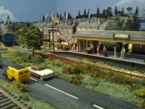 human figurines on a platform with houses in the background, waiting for the train to arrive