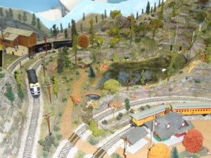 trains running through the tracks with houses, a mountain, and a lake