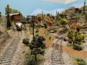 model railroad with trees and backdrop of blue skies and clouds