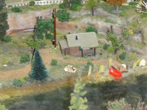 cabin by lake with red boat and wooden deck on a model railroad