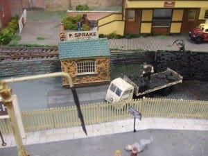 Coal truck beside a brick house and yellow-and-brown building.