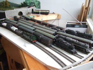 Model trains gathered on top of a white board with train tracks. 