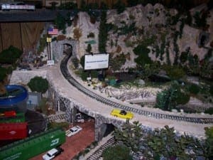 American flag beside a tunnel entrance and a yellow car driving beside the train track.