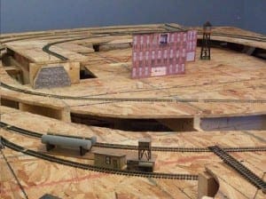 Front of a red building, a water tower, and train tracks on a wooden table. 