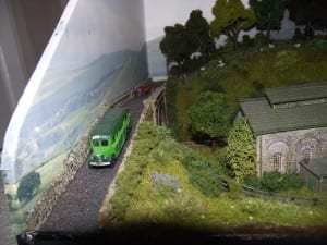 Green truck driving down narrow road beside the end of the layout.