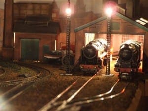 Two model trains parked in the garage during nighttime.