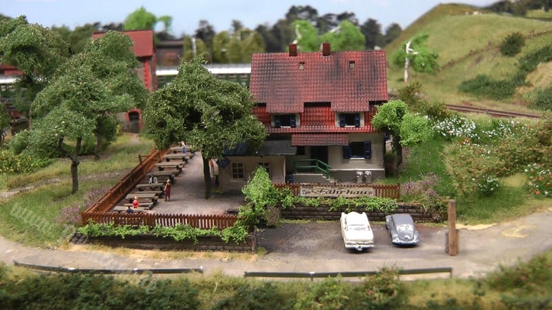 Red house on the z scale train layout with cars parked out front. 