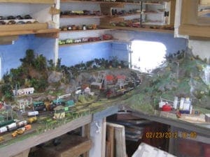 model train track on a table underneath a set of shelves which holds vehicle figurines
