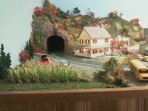 house with its lights on next to the mouth of a tunnel of this model railroad