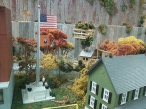 man raising flag next to school on model railroad