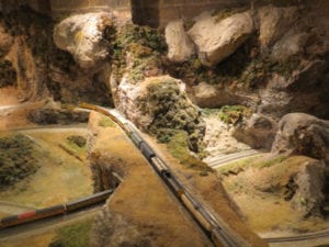 Two model trains crossing paths on separate intersecting train tracks. 