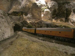Model train moving to the entrance of a rocky tunnel that leads into a mountain. 