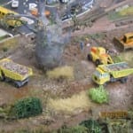 Yellow construction vehicles surrounding a car on the model railroad.