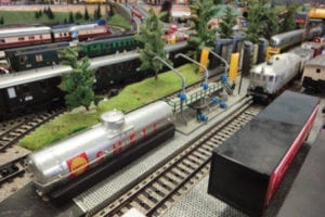 Gas tank and two train cars by the track.