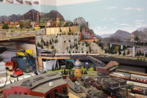 A water tower, a crane, and a tunnel with a model train in the distance; buildings fill up the scenery. 
