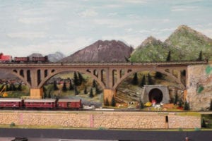 Model trains passing by tunnel with animals.