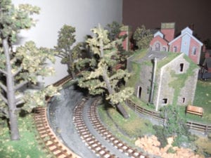 old tree and grey building beside the model train tracks