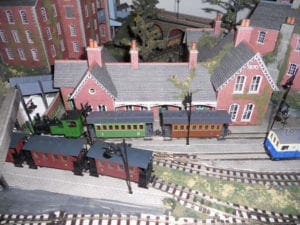 red, green, and blue-and-white trains on tracks beside buildings