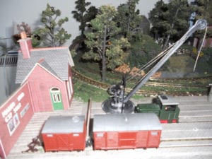 Boxcars and a crane near a red house on the model railroad layout