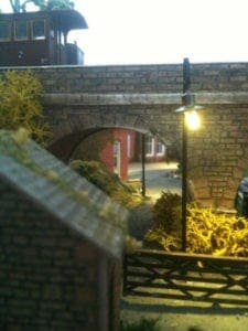 stone bridge with rail road track on top and red houses seen through the bridge's arc. 