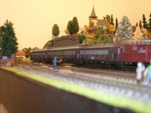 A church on the hill overlooking the railroad tracks with people watching the train go by. 
