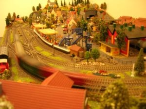 Model train coming to a curve during sunset with houses and trees in the background.