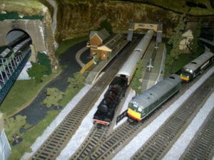 Platform and houses next to trains coming out of the tunnel of model railroad
