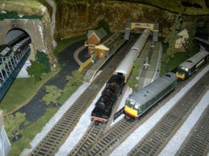 Platform and houses next to trains coming out of the tunnel of model railroad