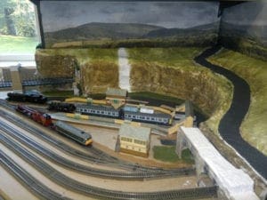 railroad model with mountain backdrop and unpainted bridge