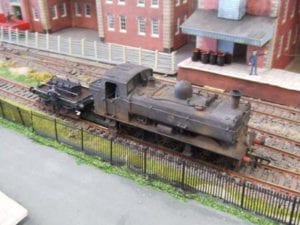 Close up look of the weathered locomotive by a fence and houses. 