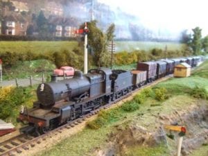 A weathered model train passing by trees and grass.
