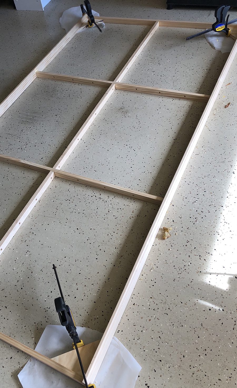 Model railroad benchwork frame being clamped square on a garage floor with bar clamps at the corners