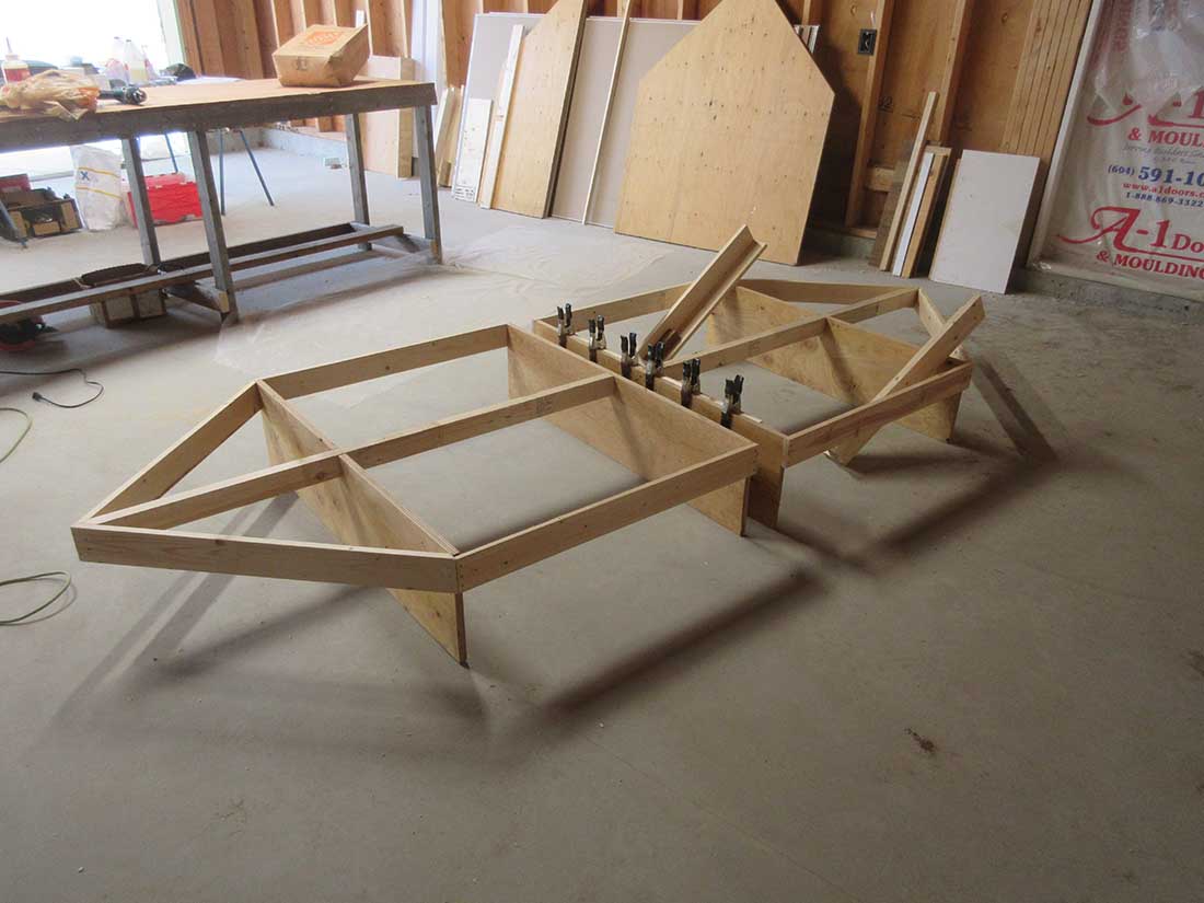 Bare plywood model train table on trestle legs with bracing, under construction in a workshop