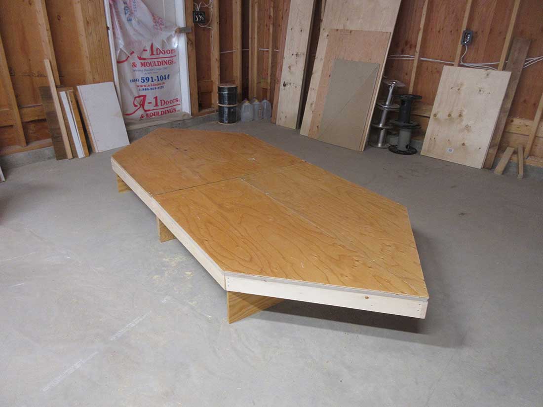 Model train table with plywood top being fitted over an open grid frame in a workshop