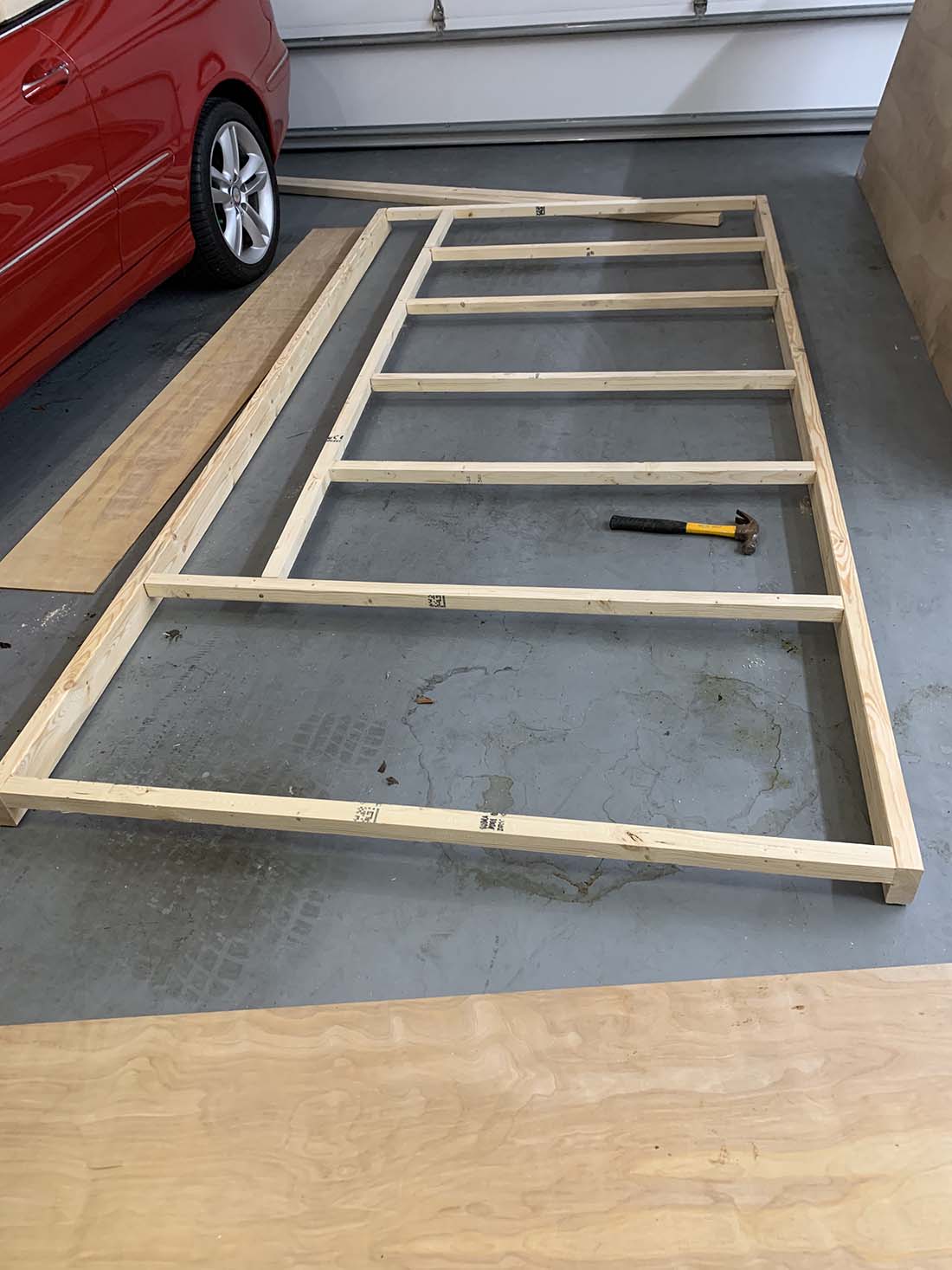 Open grid model train table frame made from 1x4 lumber laid out on a garage floor with a hammer