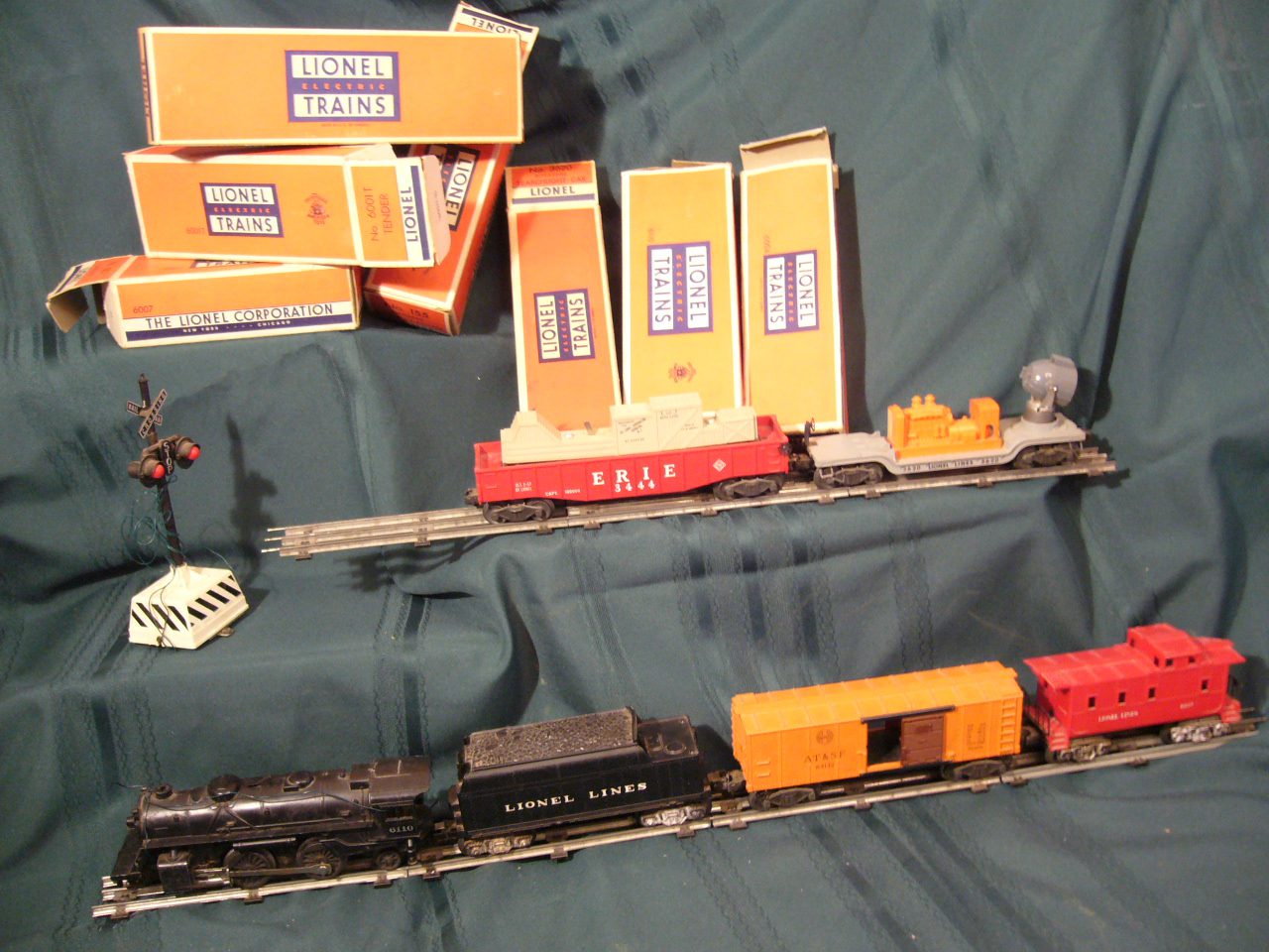 A vintage Lionel O gauge steam train with boxcar and caboose on three-rail track beside original Lionel boxes